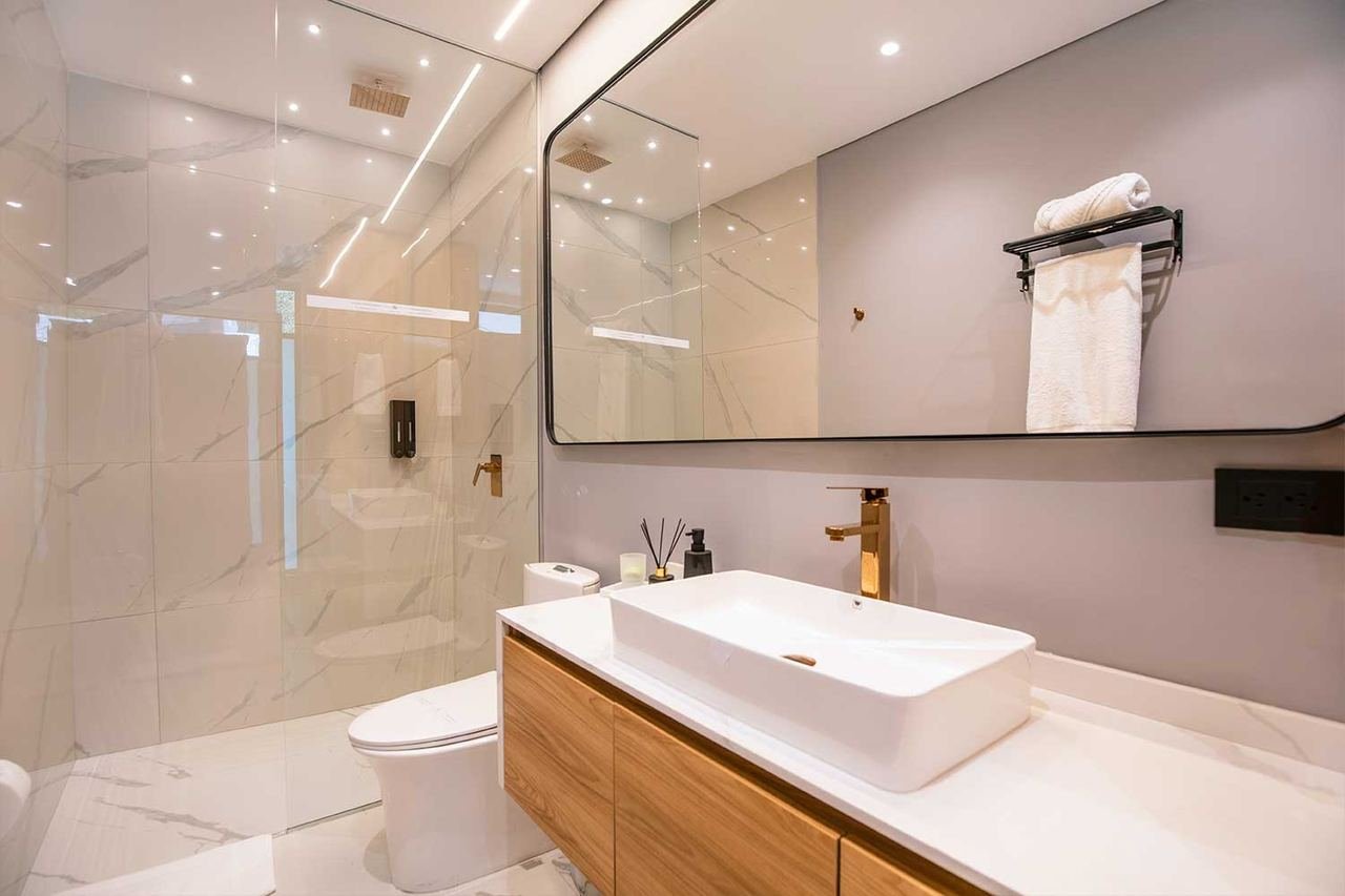 Baño con lavamanos sobre mueble en madera y ducha en vidrio