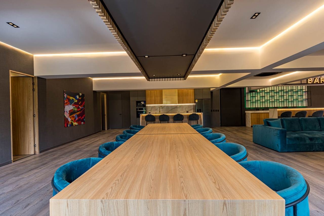Comedor con mesa larga en madera, sillas tapizadas y cielo raso con luz indirecta
